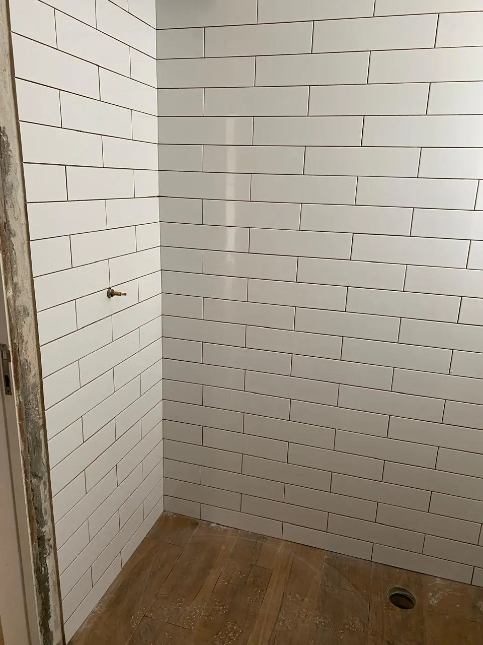 Banheiro com revestimento subway branco e piso amadeirado
